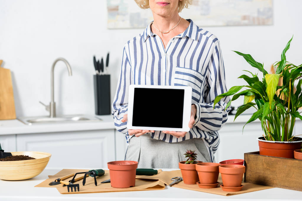 cropped shot of senior woman holding digital tablet with blank screen while cultivating plants at home - Photo, Image