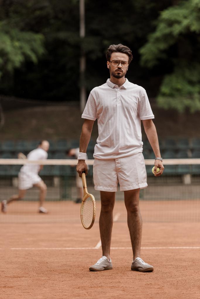 jugador de tenis de estilo retro de pie con raqueta y pelota en la cancha
 - Foto, Imagen