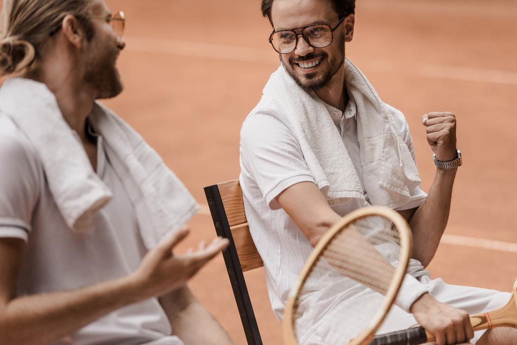 sonrientes jugadores de tenis de estilo retro sentados en sillas y hablando en la cancha de tenis
  - Foto, imagen