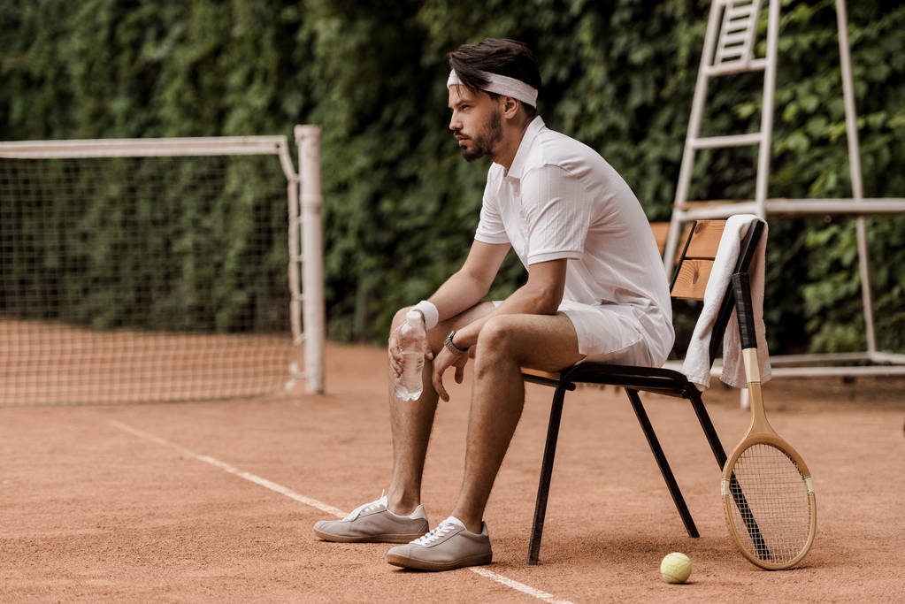 vista lateral de bonito retro estilo tenista sentado na cadeira com garrafa de água no campo de ténis
  - Foto, Imagem