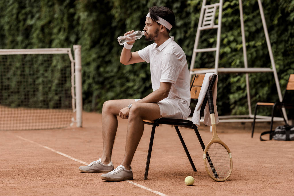 przystojny retro stylu tenisista, siedząc na krześle i wody pitnej o kort tenisowy - Zdjęcie, obraz