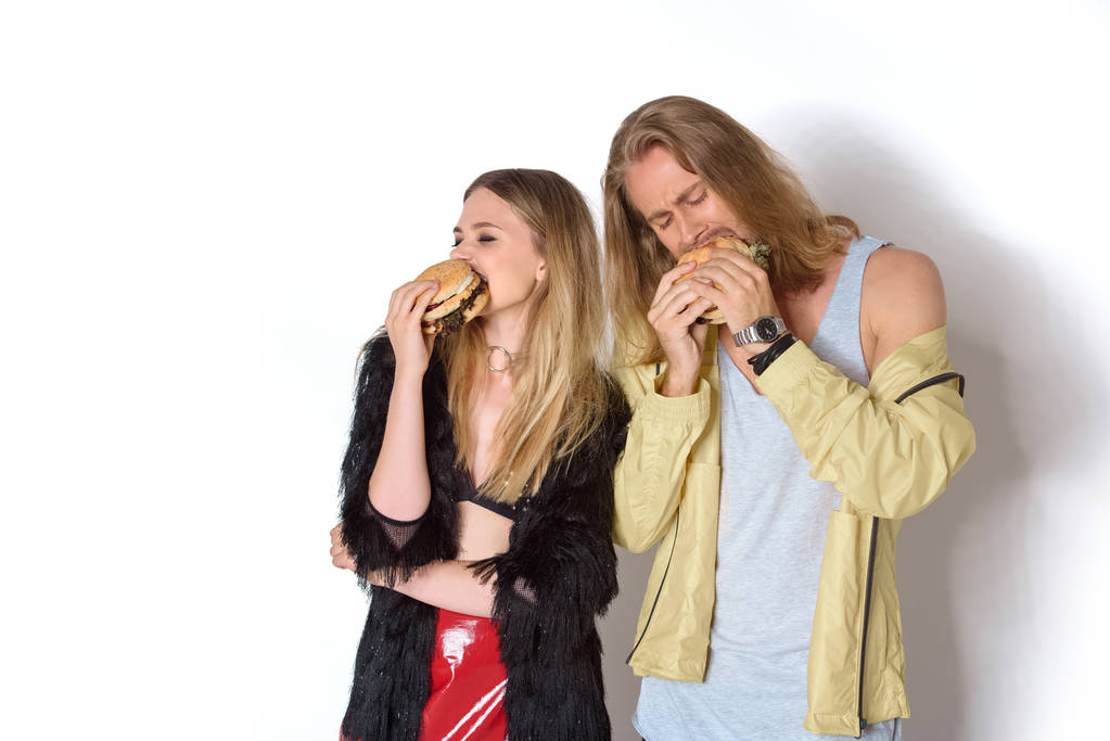 jovem casal faminto comer hambúrgueres saborosos em branco
 - Foto, Imagem