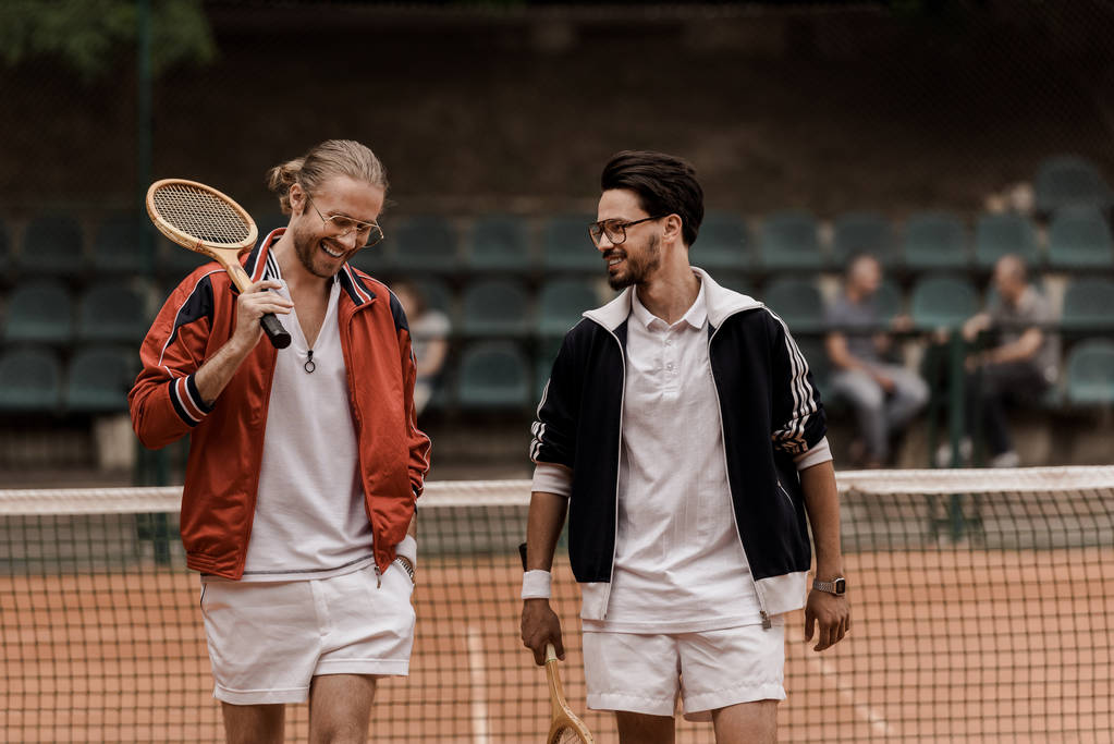 sonrientes jugadores de tenis de estilo retro caminando con raquetas en la cancha de tenis
   - Foto, imagen