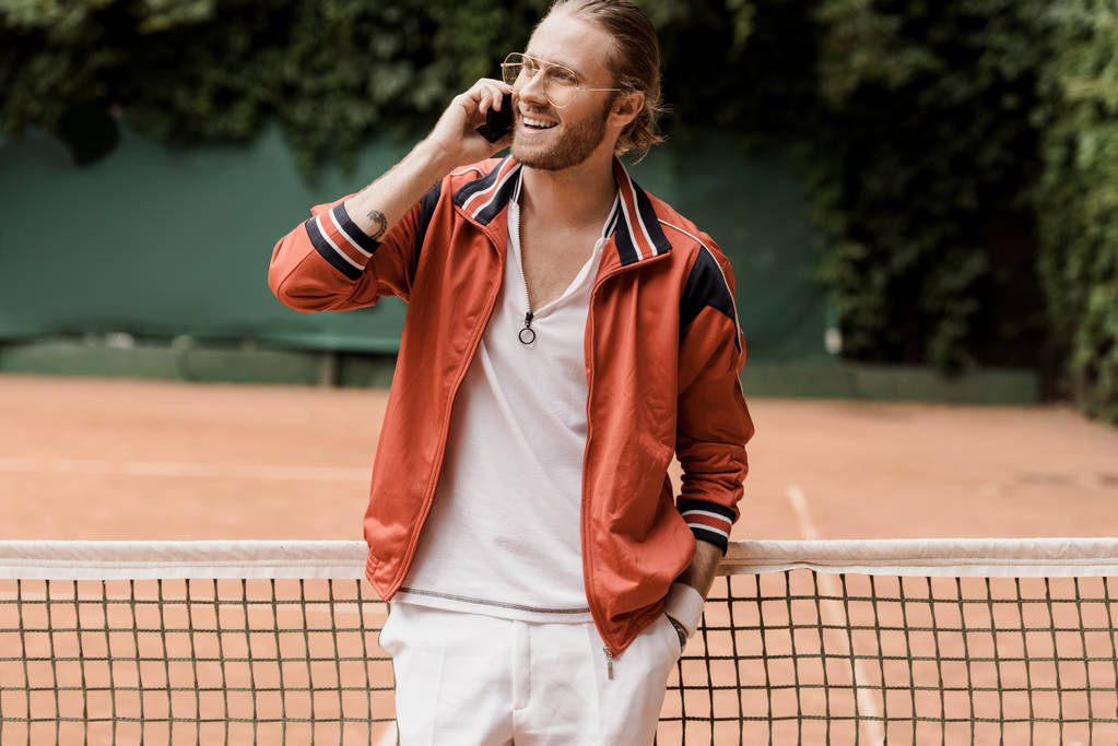sonriente jugador de tenis estilo retro hablando por teléfono inteligente en la cancha de tenis
 - Foto, imagen