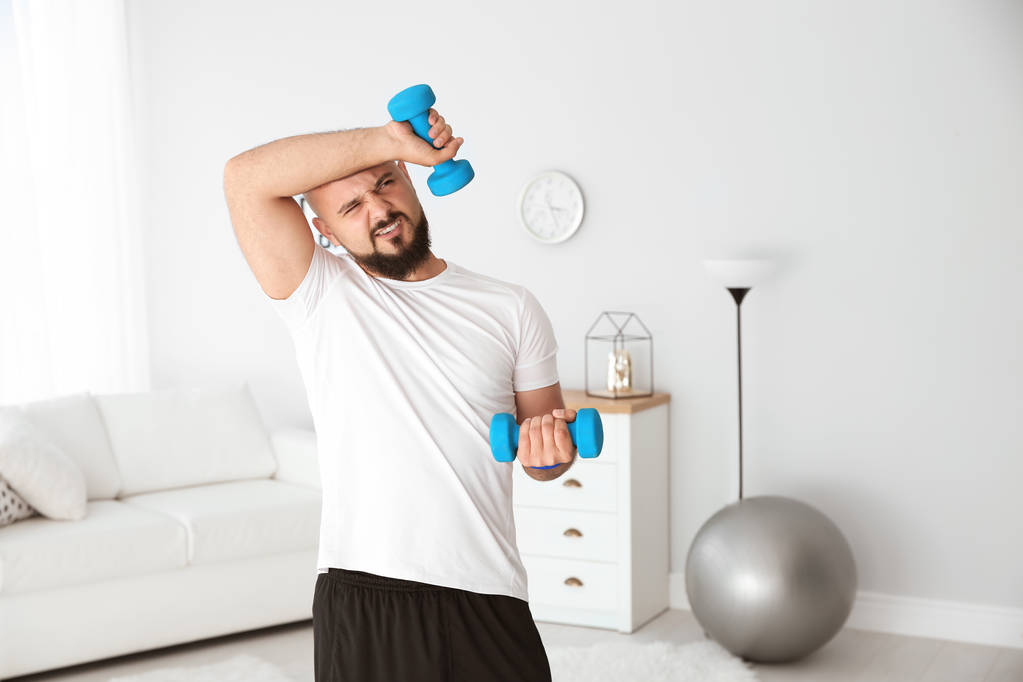 Moe overgewicht man doen oefening met halters thuis - Foto, afbeelding