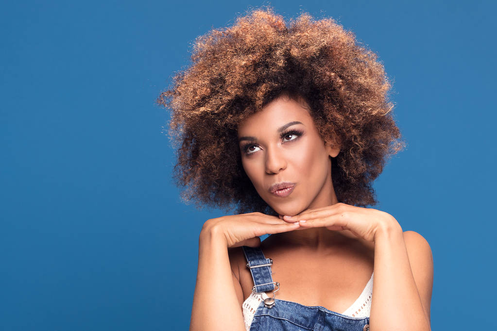 Portrait de beauté de femme afro-américaine avec maquillage glamour et coiffure afro. Fille levant les yeux, posant sur fond bleu
. - Photo, image