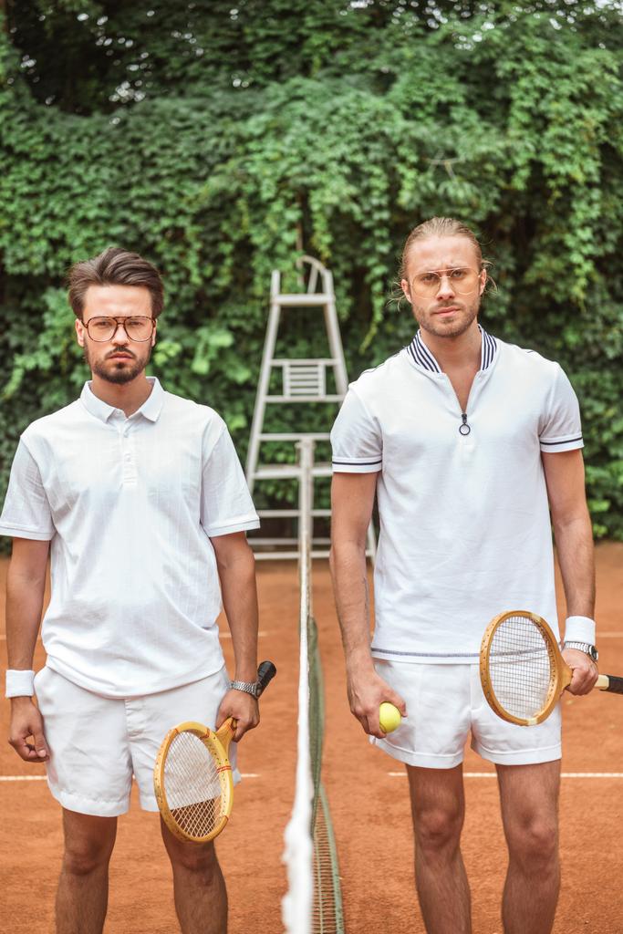 serious sportsmen with wooden rackets and ball posing after game on tennis court  - Photo, Image