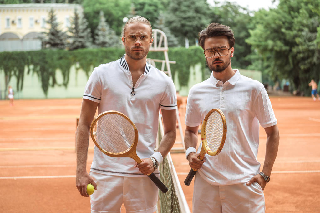 ernsthafte Tennisspieler mit Holzschlägern und Ball posieren nach dem Spiel auf dem Platz  - Foto, Bild