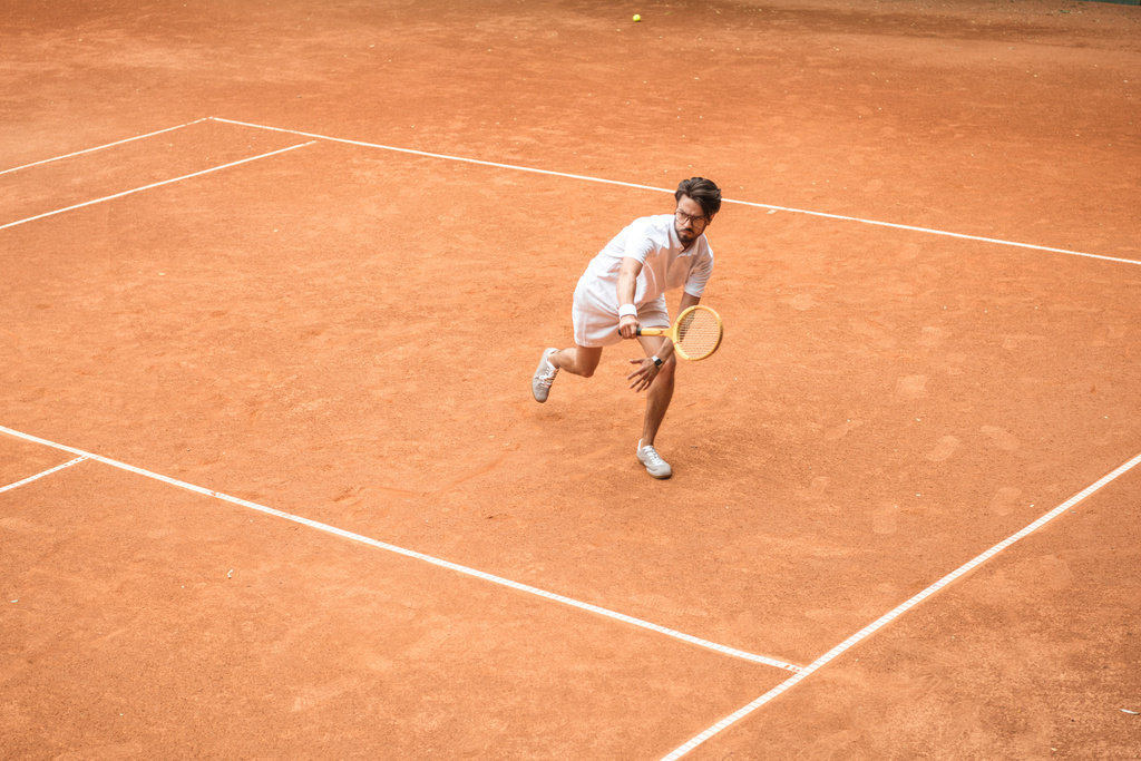 knappe tennisser training met houten racket op bruin Hof - Foto, afbeelding