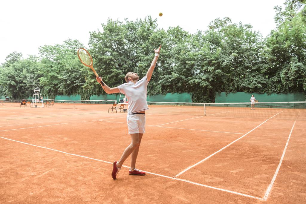 schöner Tennisspieler mit Schläger beim Ballwurf auf dem Tennisplatz  - Foto, Bild