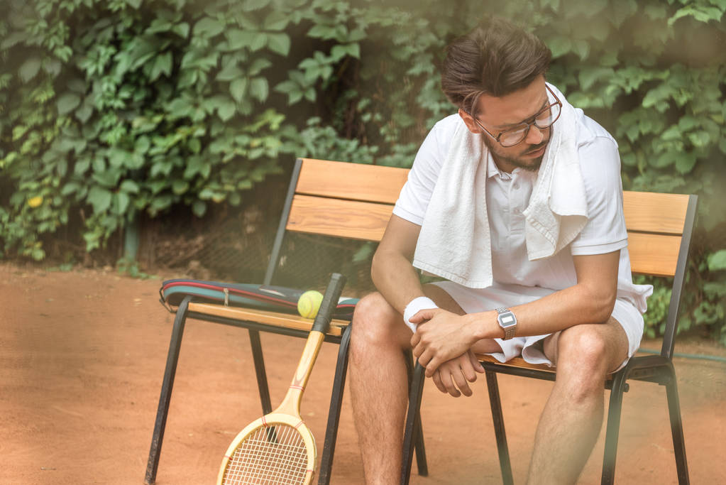 κουρασμένος τενίστας με πετσέτα και το τένις ρακέτα ακουμπά στην καρέκλα στο γήπεδο τένις  - Φωτογραφία, εικόνα