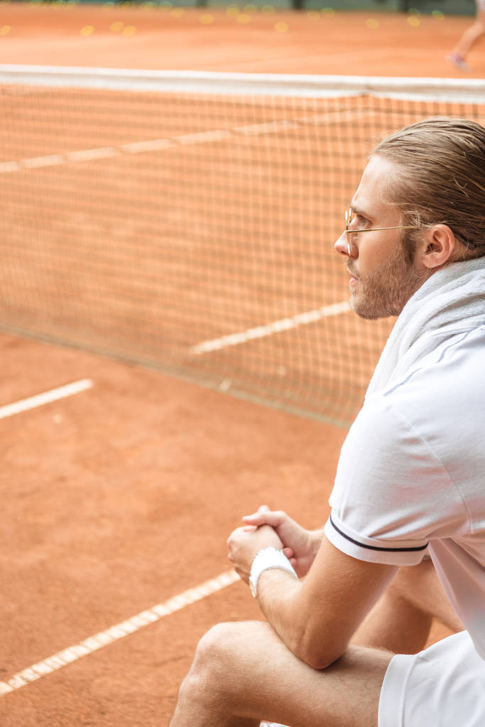 jugador de tenis anticuado con toalla descansando en cancha de tenis marrón con red
 - Foto, imagen