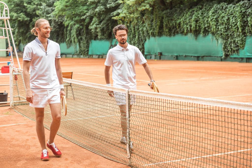 jogadores de tênis com raquetes de madeira andando depois de treinar perto da rede na quadra
 - Foto, Imagem