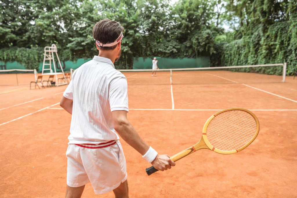 πίσω όψη του αθλητή παίζοντας τένις με ξύλινη ρακέτα στο γήπεδο τένις - Φωτογραφία, εικόνα