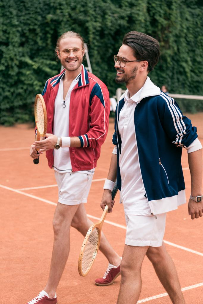 sorridenti amici in stile retrò con racchette di legno che camminano sul campo da tennis
 - Foto, immagini