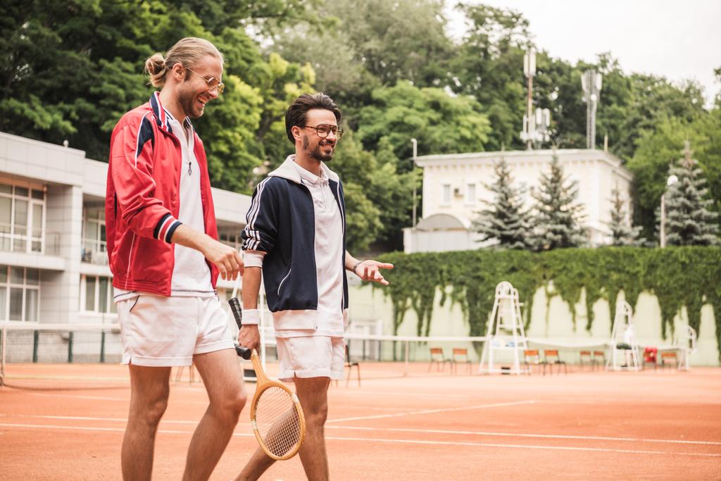 smiling friends with wooden rackets walking on tennis court - Photo, Image