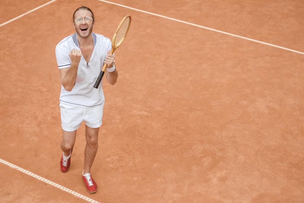 guapo ganador emocional con raqueta gritando y celebrando en la cancha de tenis
 - Foto, Imagen
