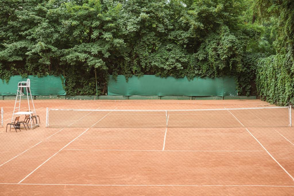 вид на коричневий тенісний корт зі стільцями та тенісною мережею
 - Фото, зображення