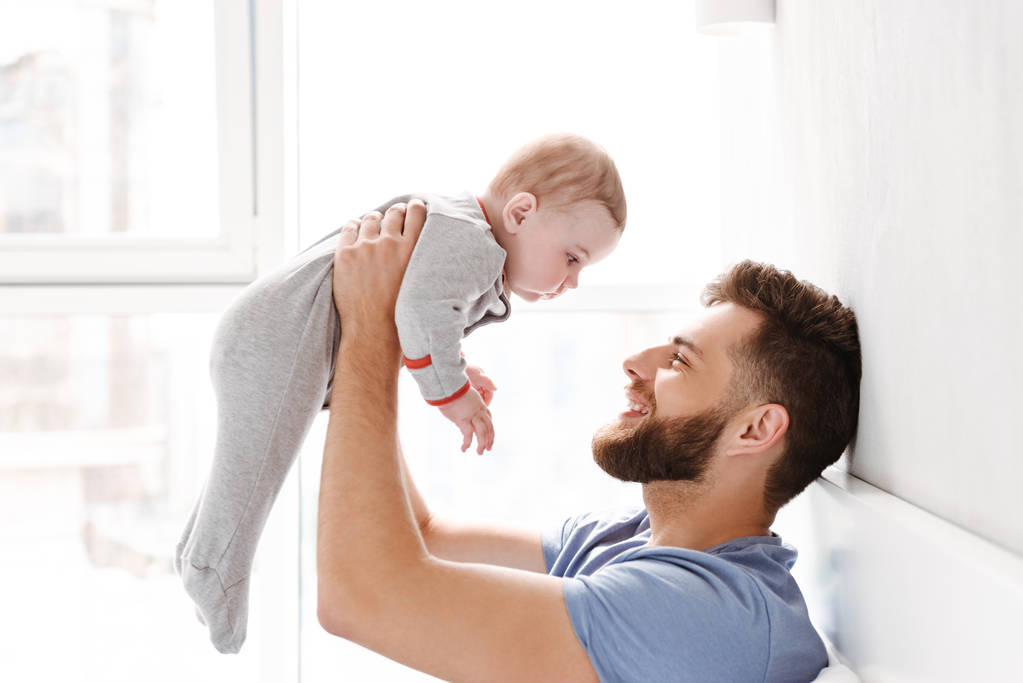 Φωτογραφία του χαρούμενος νεαρός πατέρας μπαμπά διασκεδάζοντας με τον μικρό γιο του μωρού παιδιού σε κλειστούς χώρους στο σπίτι. - Φωτογραφία, εικόνα