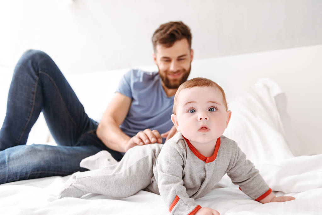 Foto de guapo feliz joven padre padre papá divirtiéndose con su pequeño hijo bebé hijo en el interior en casa
. - Foto, imagen