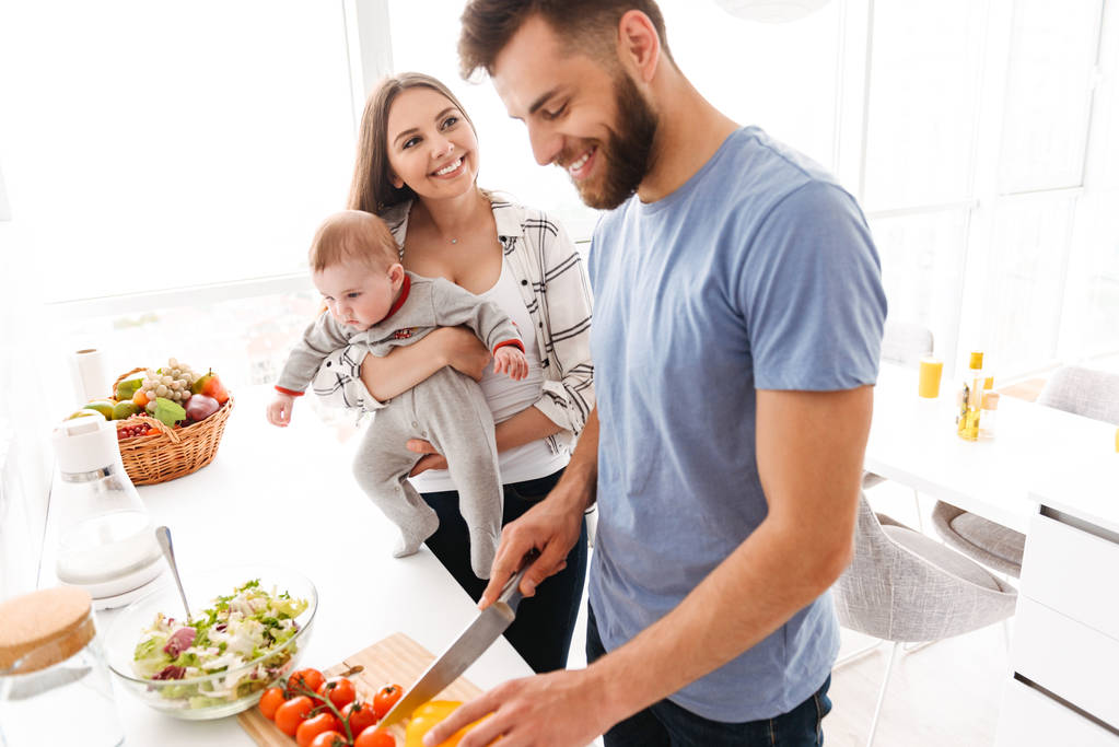 Kép a boldog fiatal szerető pár szülők-val a kis gyerek baba fiuk konyhában főzés. - Fotó, kép