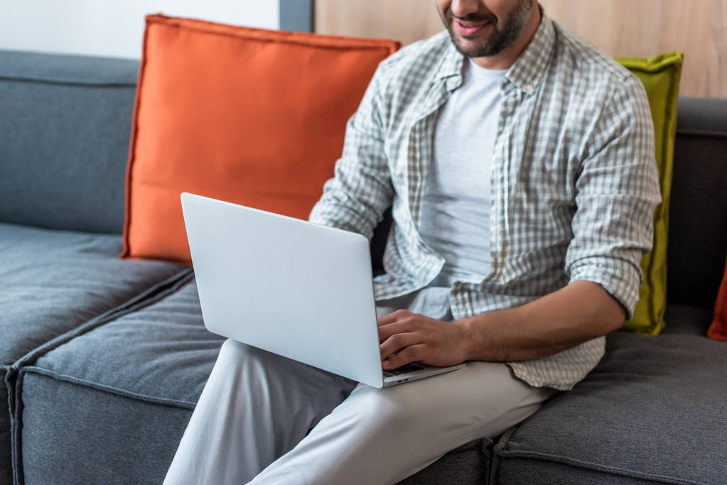 partial view of smiling man using laptop on couch at home - Photo, Image