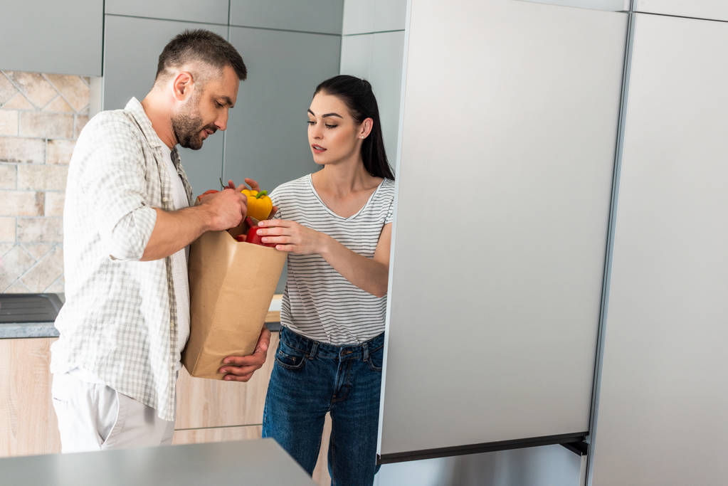 married couple putting fresh vegetables into fridge in kitchen at home - Photo, Image