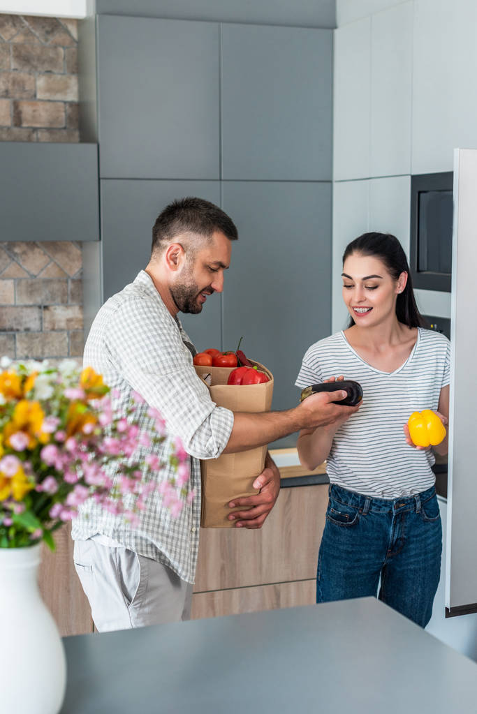 笑顔の結婚されていたカップルが自宅の台所で冷蔵庫に新鮮な野菜を入れて - 写真・画像