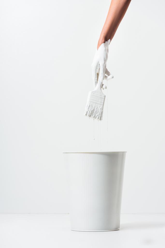 abgeschnittenes Bild einer Frau, die einen Pinsel mit weißer Farbe über einem Eimer auf Weiß hält - Foto, Bild