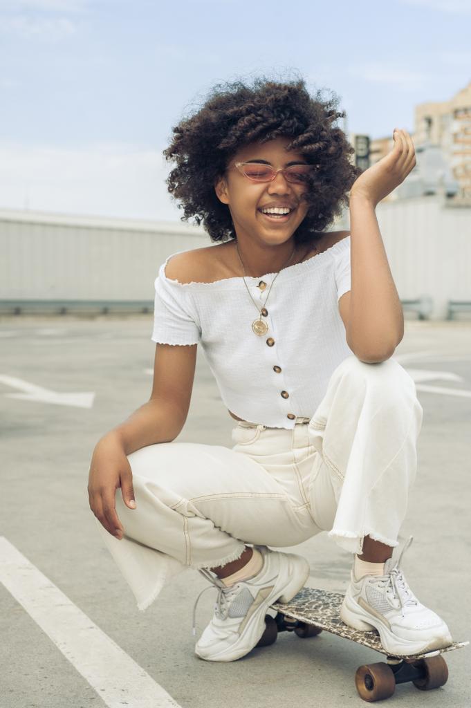 kaykay üzerinde çömelmiş ve sokakta gülerek mutlu genç Afro-Amerikan kadın - Fotoğraf, Görsel