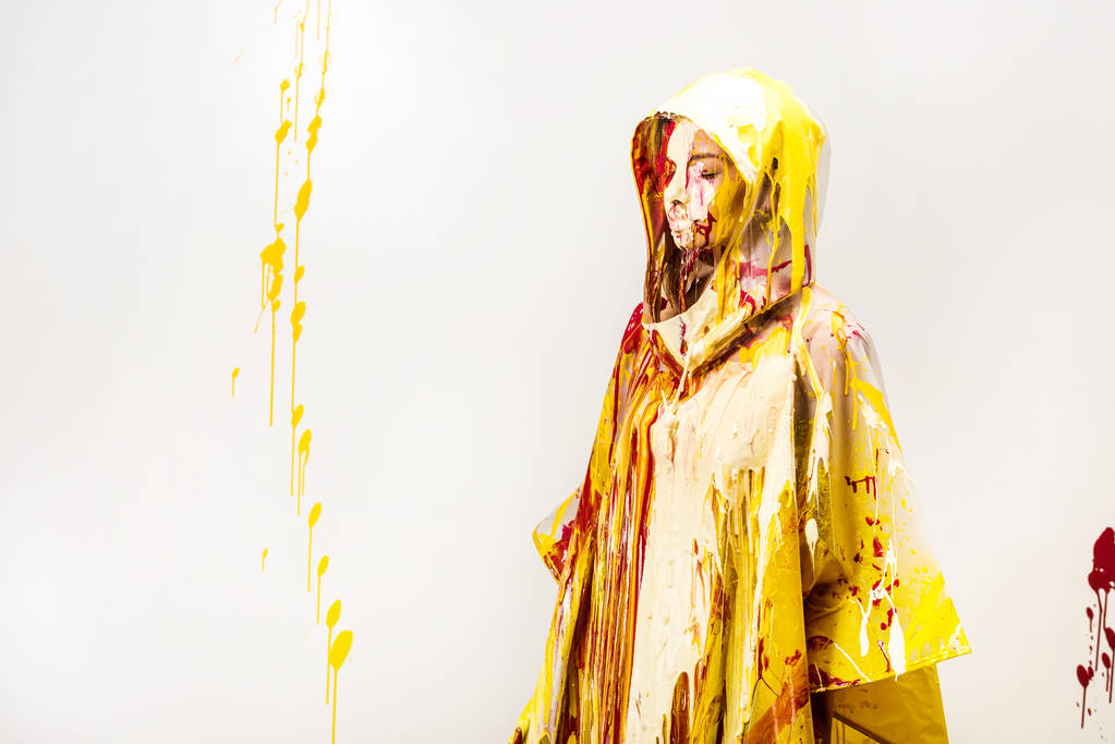 schöne Frau im Regenmantel mit gelben und roten Farben bemalt stehend in Kapuze isoliert auf weiß - Foto, Bild