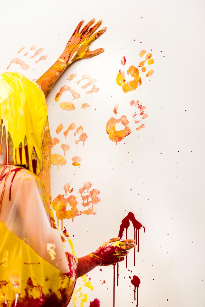 Frau im Regenmantel bemalt Wand mit gelben und roten Handabdrücken - Foto, Bild