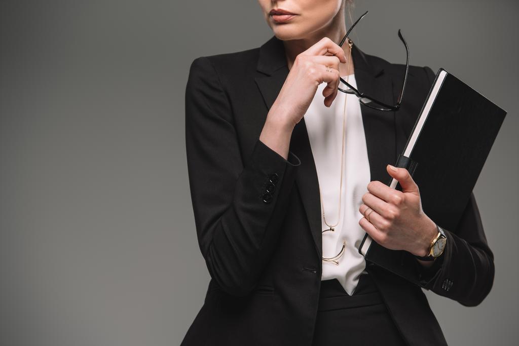 обрізане зображення бізнес-леді, що тримає окуляри та підручник ізольовані на сірому фоні
  - Фото, зображення