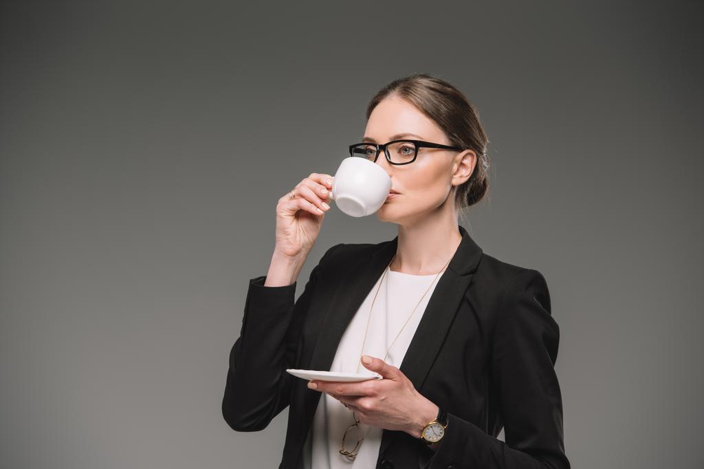 Geschäftsfrau in Brille trinkt Kaffee aus Tasse isoliert auf grauem Hintergrund  - Foto, Bild