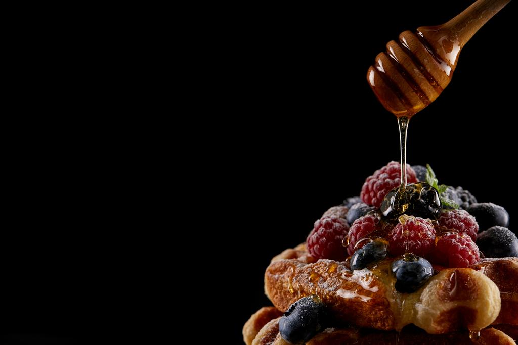 miel vertiendo sobre deliciosos gofres belgas aislados en negro
 - Foto, imagen