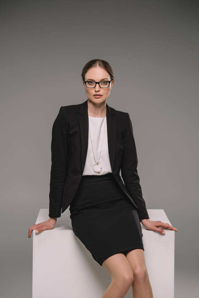 приваблива бізнес-леді в окулярах, сидячи на кубі на сірому фоні
  - Фото, зображення