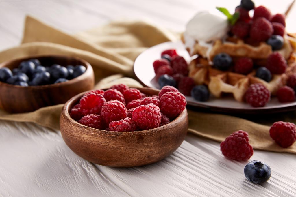bowls with berries with belgian waffles blurred on background on white wooden table - Photo, Image