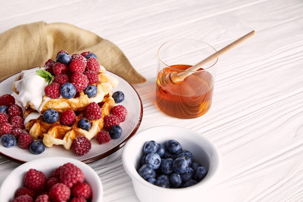 вкусные бельгийские вафли с ягодами и медом на белом деревянном столе
 - Фото, изображение