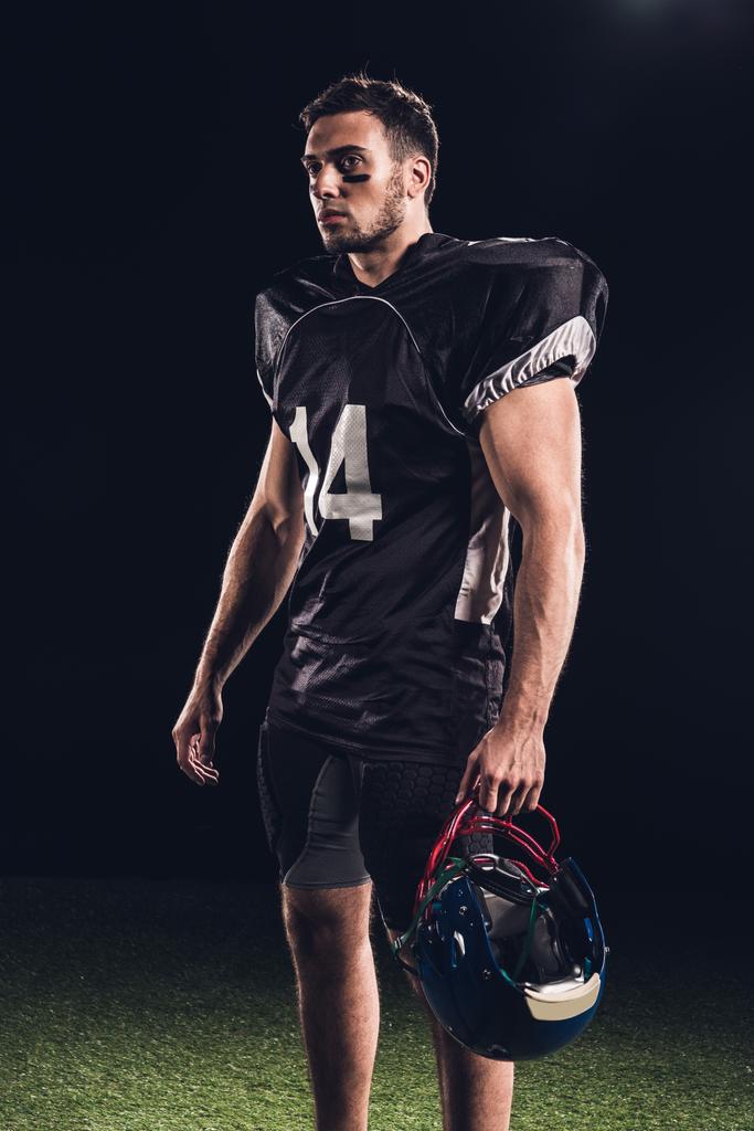 atlético jugador de fútbol americano en uniforme negro con casco y mirando hacia otro lado en negro
 - Foto, Imagen
