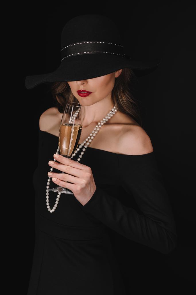 elegante vrouw met ogen vallende zwarte stro holding champagne glas geïsoleerd op zwarte achtergrond  - Foto, afbeelding