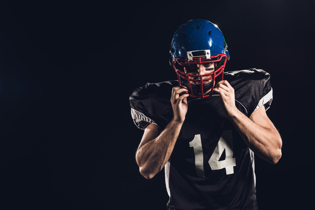 jugador de fútbol americano que se pone el casco y mira a la cámara aislada en negro
 - Foto, imagen