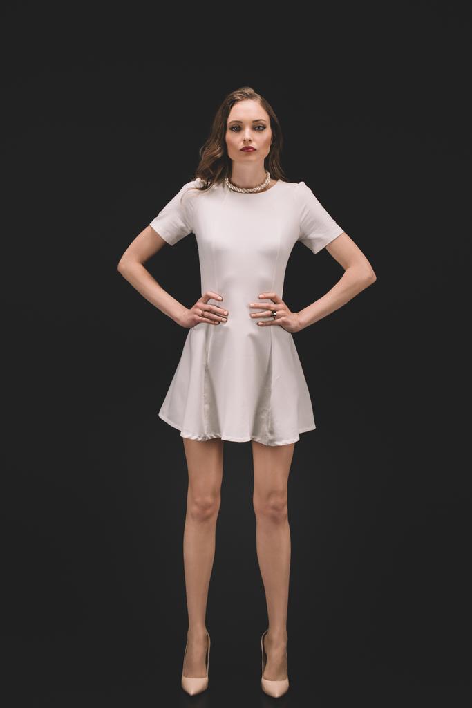 bela modelo feminina no vestido de pé com as mãos sobre os quadris isolados no fundo preto
  - Foto, Imagem