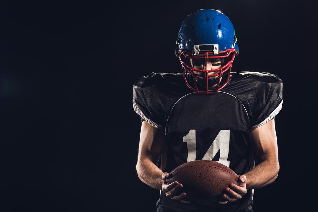 joueur de football américain regardant le ballon dans les mains isolé sur noir
 - Photo, image
