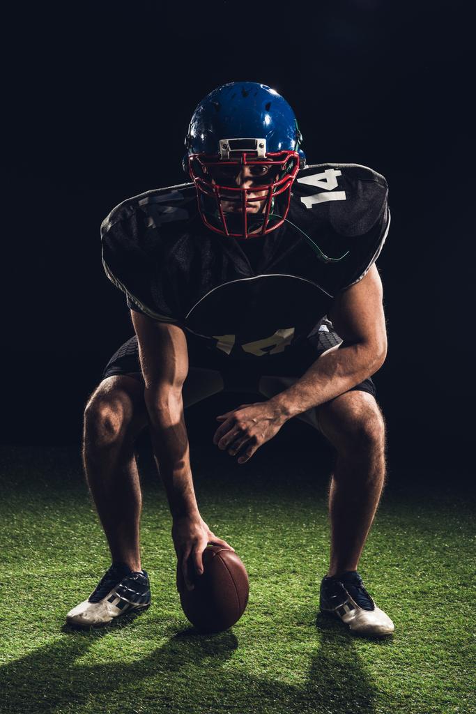 sérieux joueur de football américain debout sur l'herbe avec balle et en regardant la caméra sur noir
 - Photo, image
