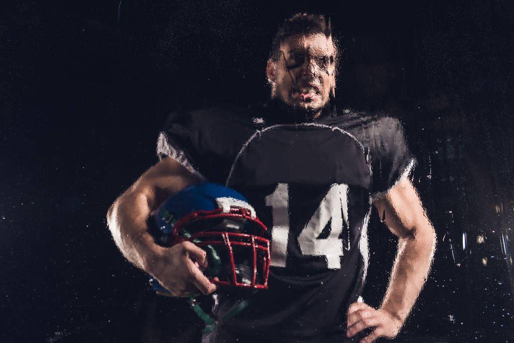 view of angry american football player with helmet on black through wet glass - Photo, Image