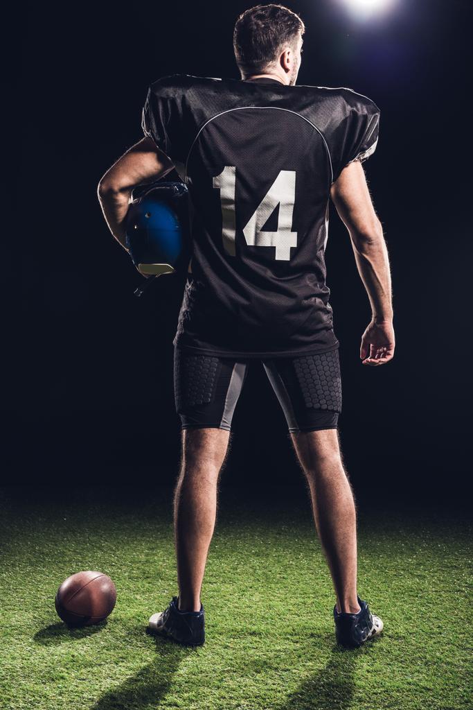 黒のヘルメット緑の草の上に立って、アメリカン ・ フットボール プレーヤーの背面図 - 写真・画像