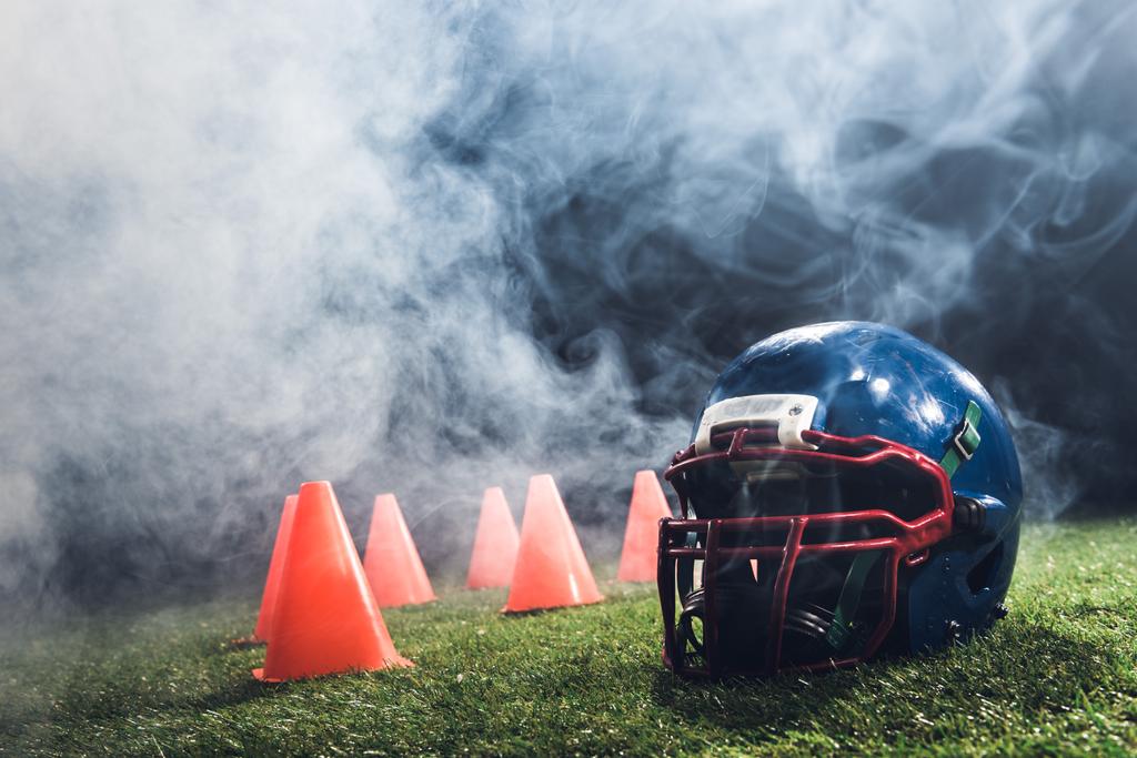 close-up shot of american football helmet with cones on green grass with white smoke above - Photo, Image