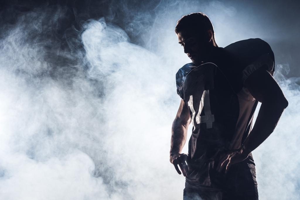 dark silhouette of thoughtful american football player looking down against white smoke - Photo, Image