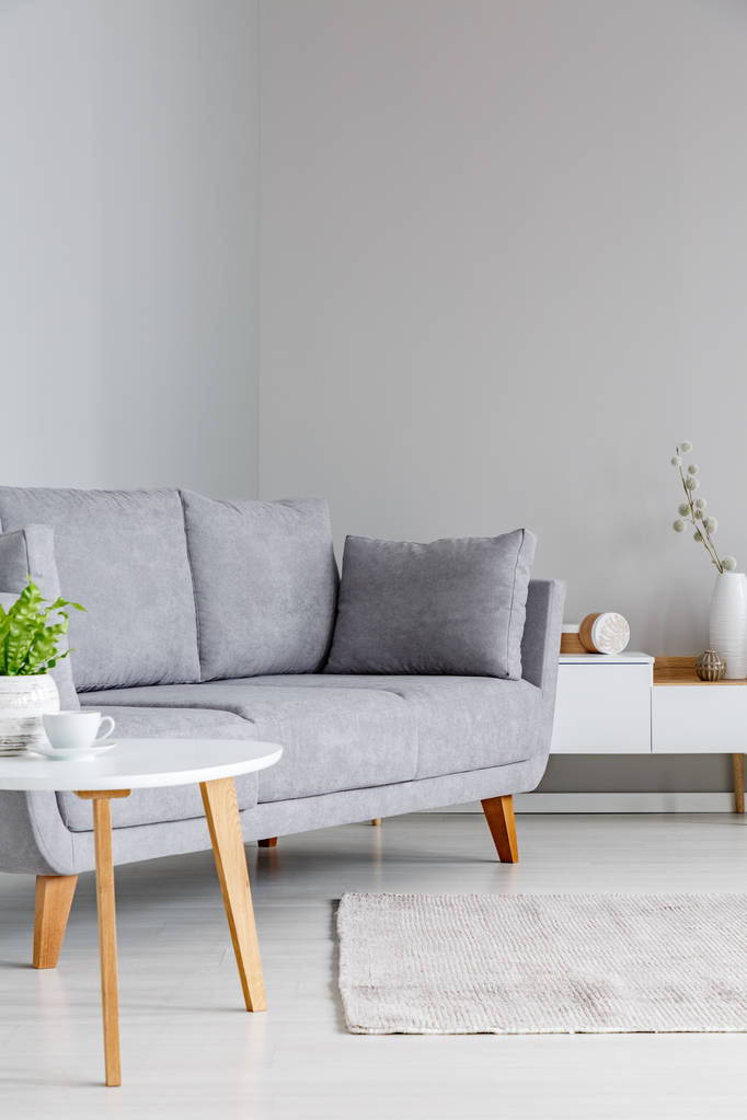 Foto real de un sofá gris entre una pequeña mesa y un armario en un interior de salón simple y gris
 - Foto, imagen