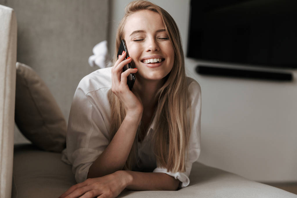Foto de una mujer joven y sonriente dentro de casa hablando por teléfono móvil
. - Foto, imagen